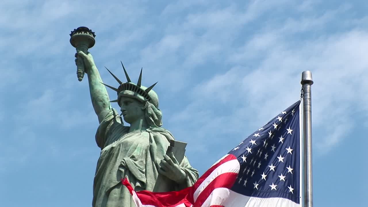 la bandera estadounidense ondea en primer plano con la estatua de la libertad orgullosamente detrás