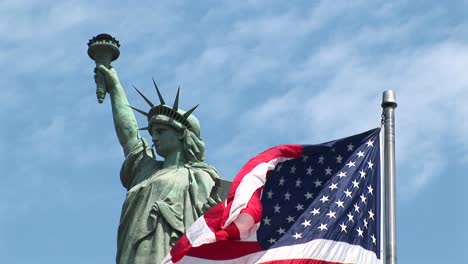 the american flag waves in the foreground with the statue of liberty standing proudly behind