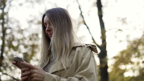 woman reading messages or surfing internet from phone at autumn park, overview footage