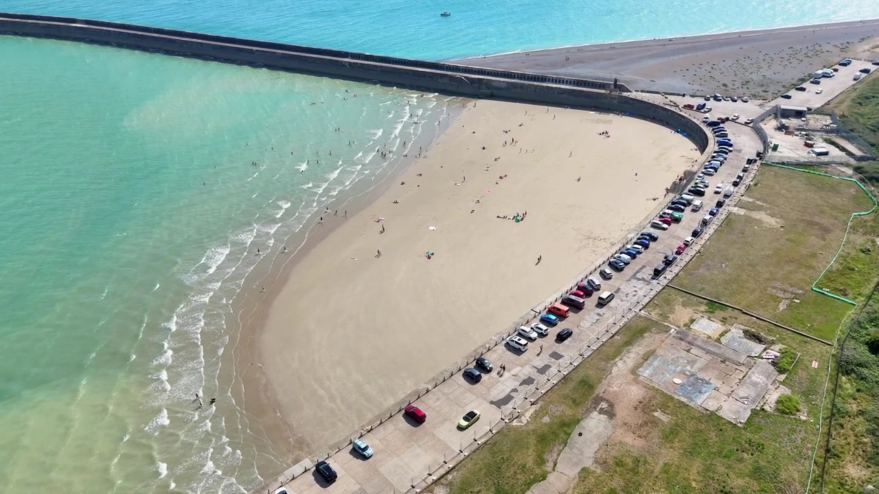 Imagens de drone da Praia Oeste fechada de Newhaven, cheia de moradores desfrutando da orla arenosa durante o verão, ao lado da entrada do porto na costa de East Sussex.