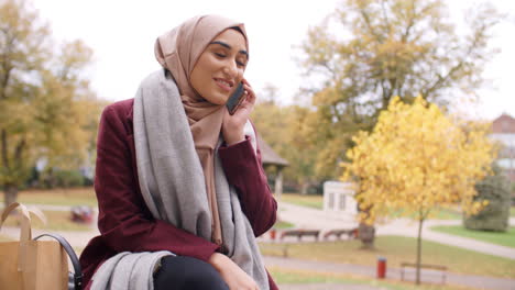 british muslim woman on break using mobile phone in park