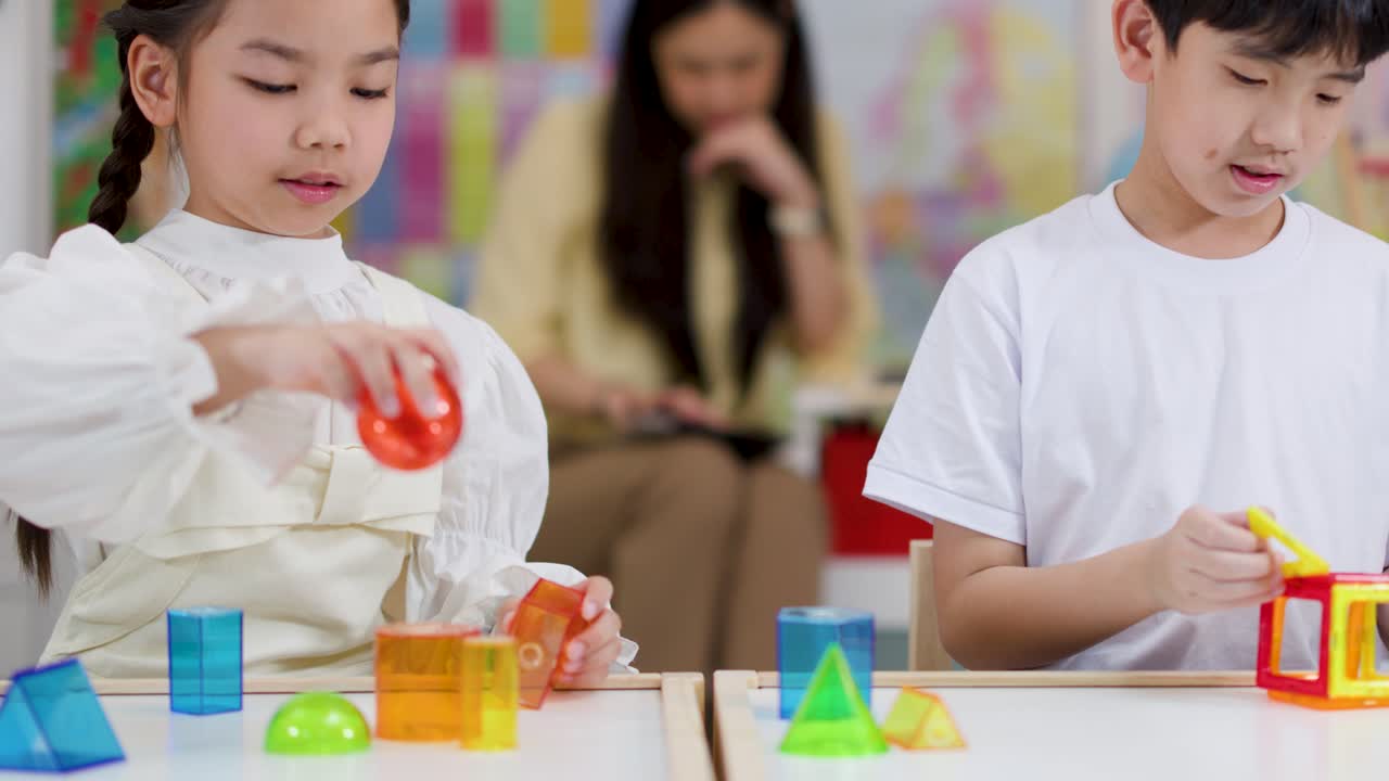 アジア系の生徒たちが、明るい教室での算数の授業で、幾何学的な立体と磁石について学んでいます。