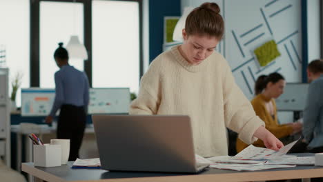 Portrait-of-focused-startup-employee-looking-at-laptop-and-charts-comparing-sales-statistics