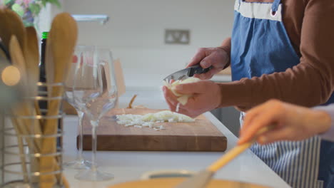 close up of couple wearing aprons chopping onions and adding them to pan as they prepare meal in kitchen together - shot in slow motion