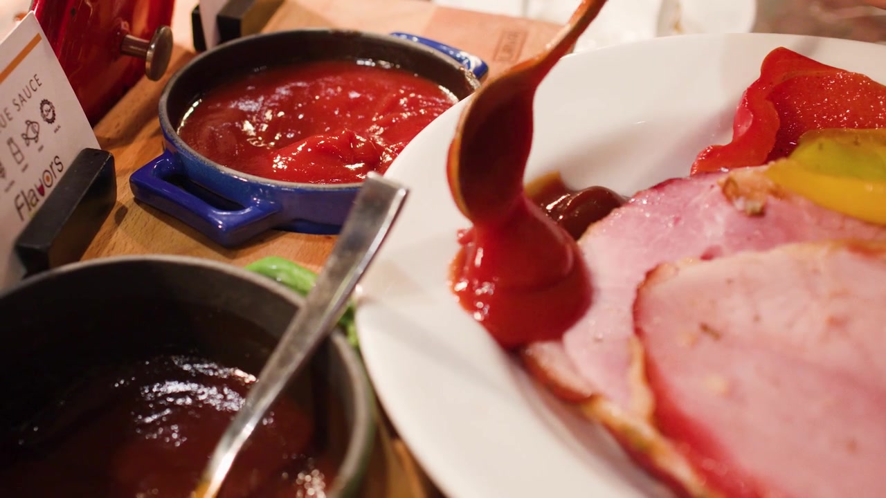 Persona che versa ketchup su prosciutto affettato su un piatto