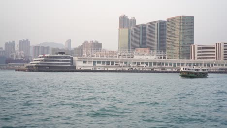 View-Of-Ocean-Terminal-With-Ferry-Boat-Sailing-Past-In-Victoria-Harbour-In-Hong-Kong