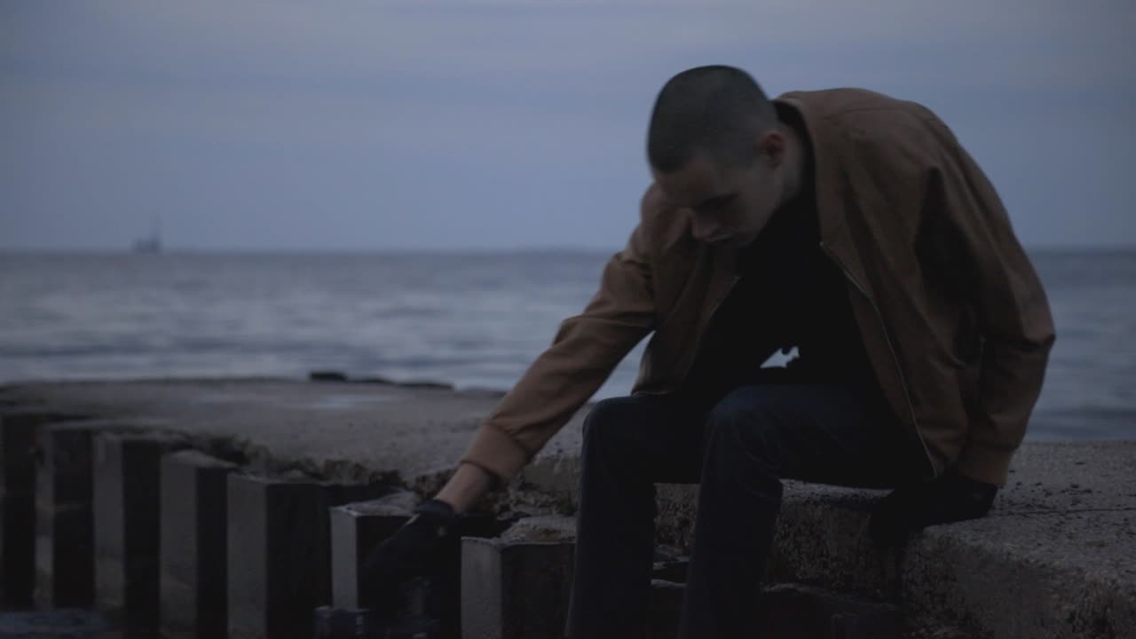 여행 사진사는 황혼의 아름다운 바다 경치를 찍기 위해 해안가의 콘크리트 제티에 앉아 있다 - 중간 샷