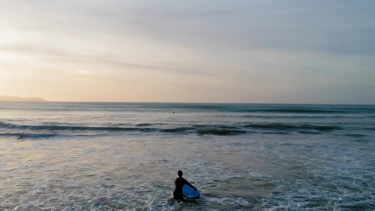 Ein Surfer trägt sein Surfbrett, um bei Sonnenuntergang ein paar Wellen zu reiten.