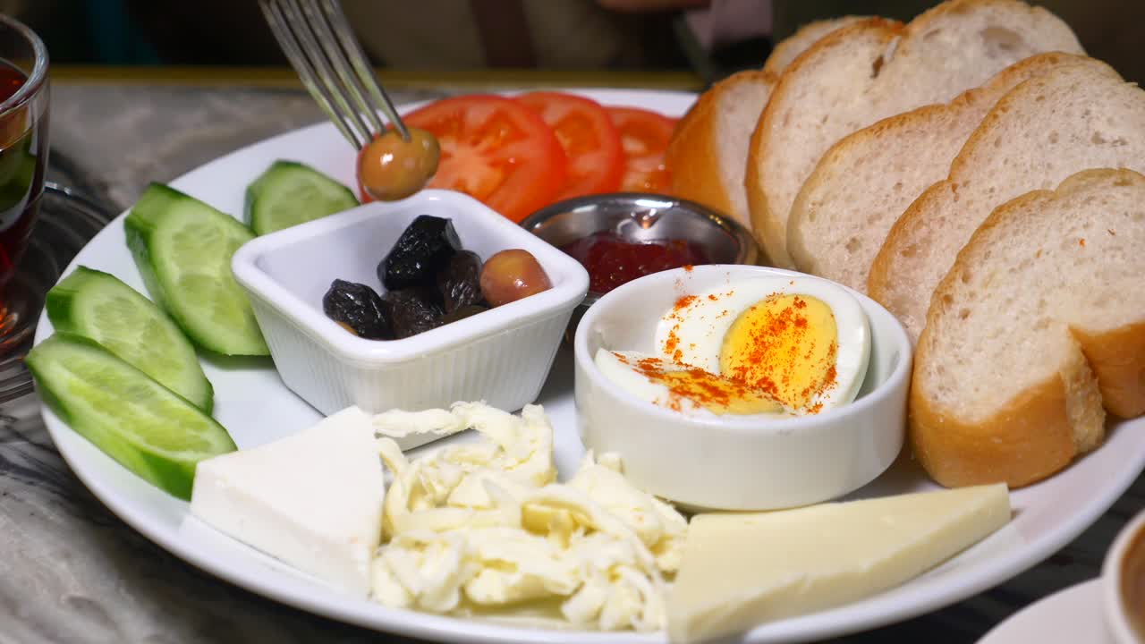 Breakfast plate with cucumbers, tomatoes, cheese, olives, egg and bread