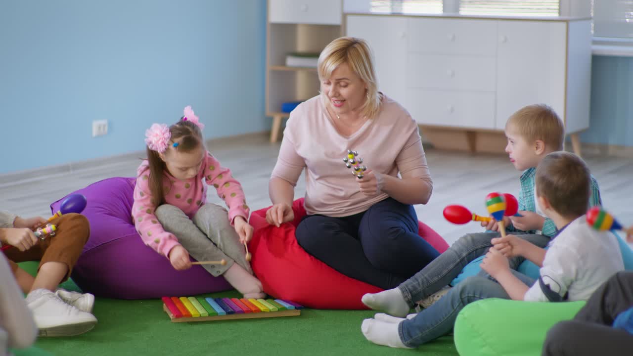 children with down syndrome in music lesson, female teacher plays musical instruments with the kids sitting on multicolored bean bag chairs