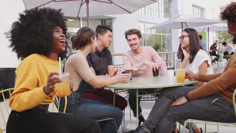 Six-trendy-millennial-friends-sitting-in-the-street-outside-a-cafe-drinking-cold-brews-and-talking