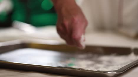 professional chef sprinkles flour on to a baking sheet