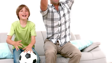 In-slow-motion-happy-father-and-son-with-football-watching-tv