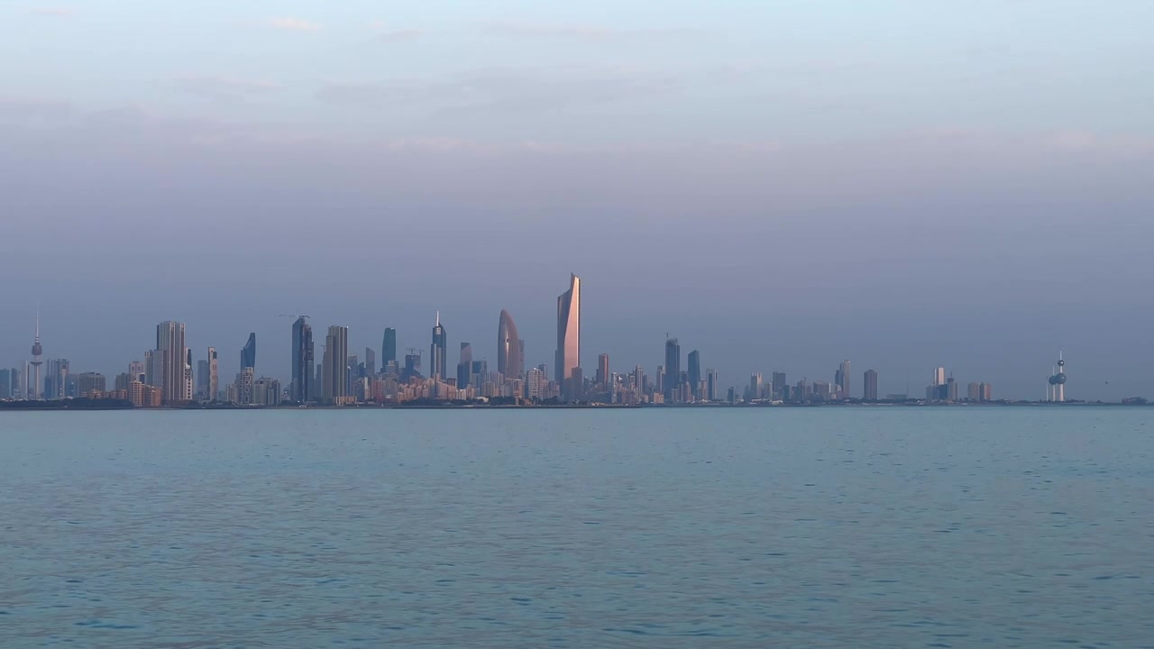 Vista estática da orla do horizonte da Cidade do Kuwait ao nascer do sol, com água do mar calma e luz matinal brilhante em 4K.