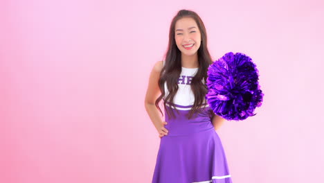 pretty asian female cheerleader with poms looking and smiling to camera