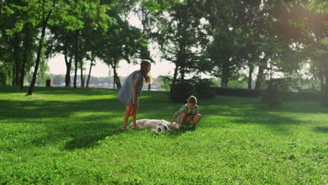 joyful siblings petting golden retriever in park. dog lying on green field.