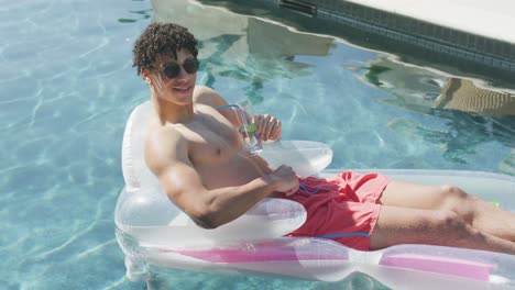 Portrait-of-happy-biracial-man-with-drink-lying-on-inflatable-in-swimming-pool-on-sunny-day