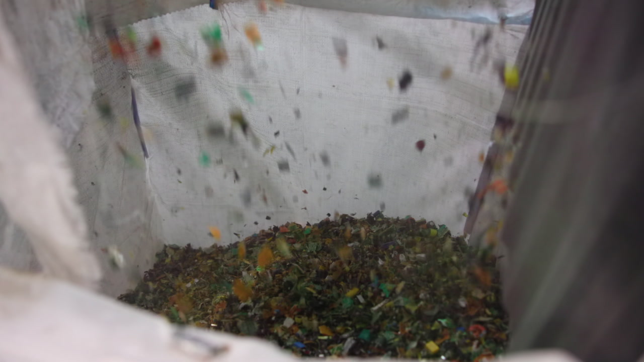 Falling Shredded Plastic Filling Bulk Bag Under Chute, Colorful Granules Cascading Into Woven Container, Dust . Media