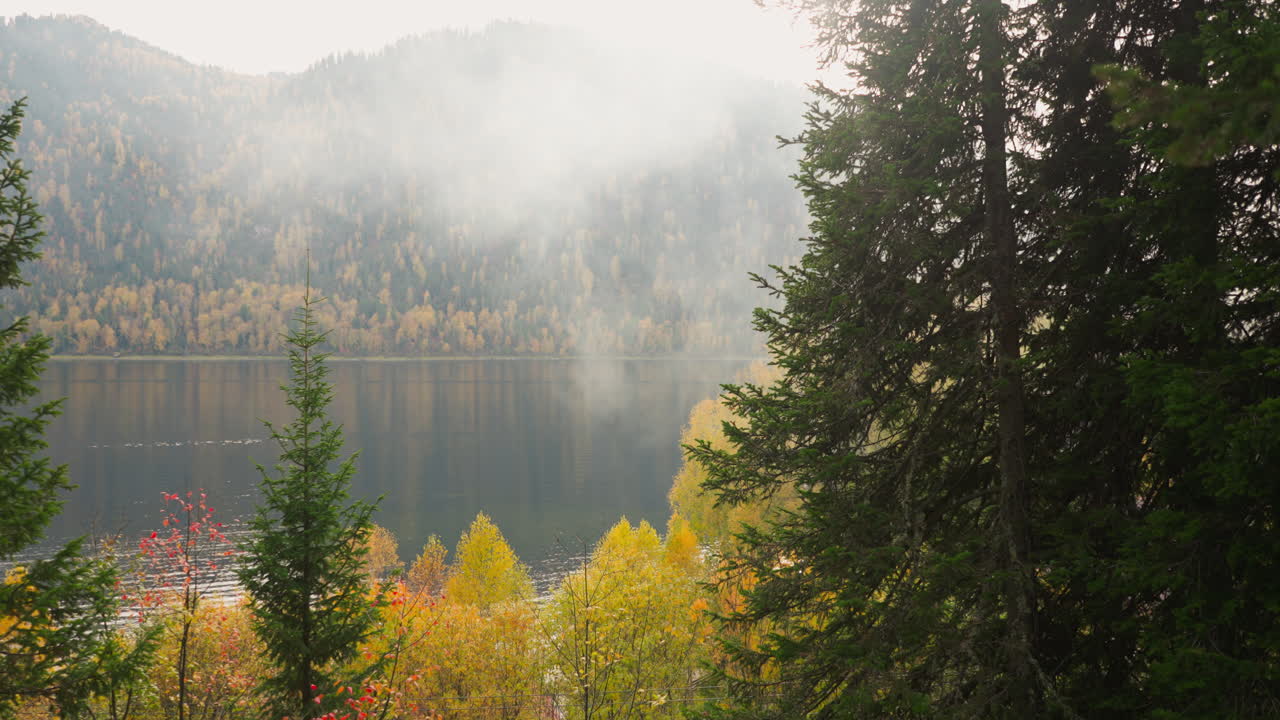 Scenic lake and mountains emerge from mist. Tourists witness gradual unveiling of nature grandeur with placid lake. Silhouette of majestic mountains