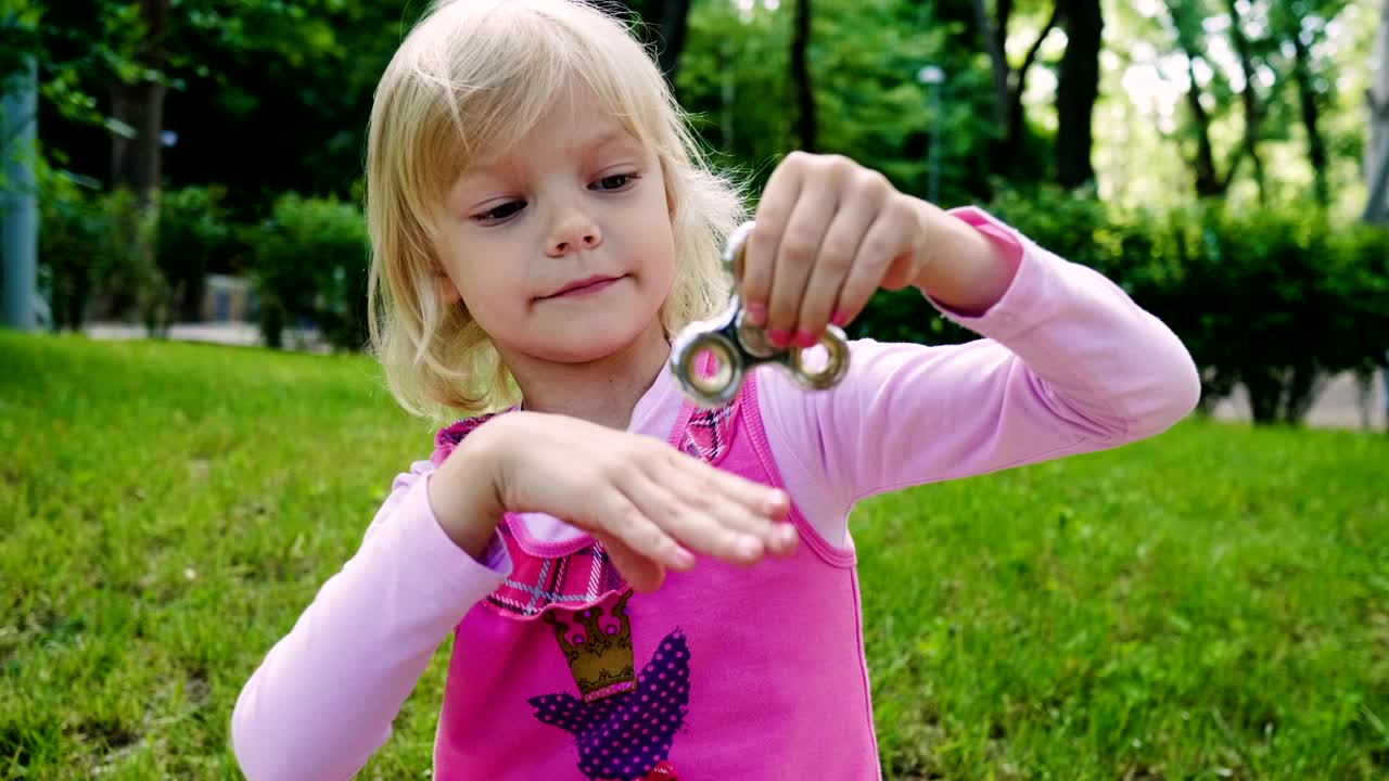 A menina loira sorridente brincando com um fidget spinner no parque. 4K