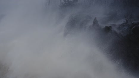 rough ocean wave crash against rocky cliff on a gloomy stormy day, slow motion