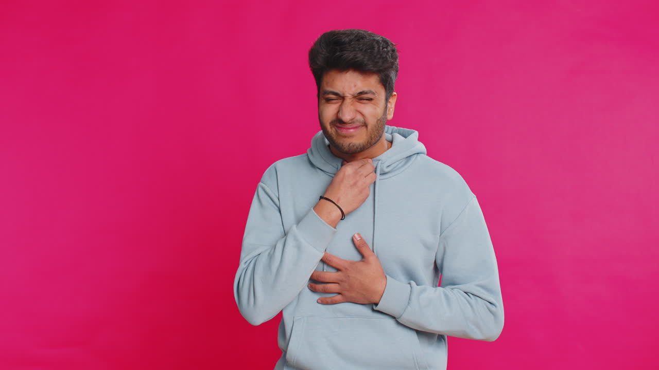 Unhealthy indian young man coughing covering mouth with hand feeling sick over pink background