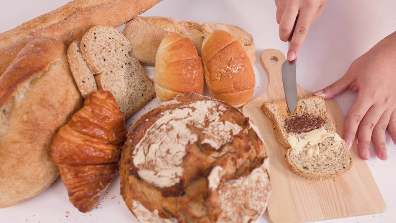 Person Spreading Chocolate Spread on Toast with Assorted Bread