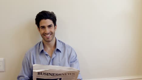 smiling man reading business newspaper at home