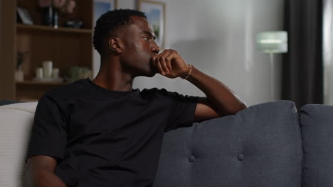 unhappy and depressed young man sitting on sofa at home looking anxious and worried resting head on hand 2