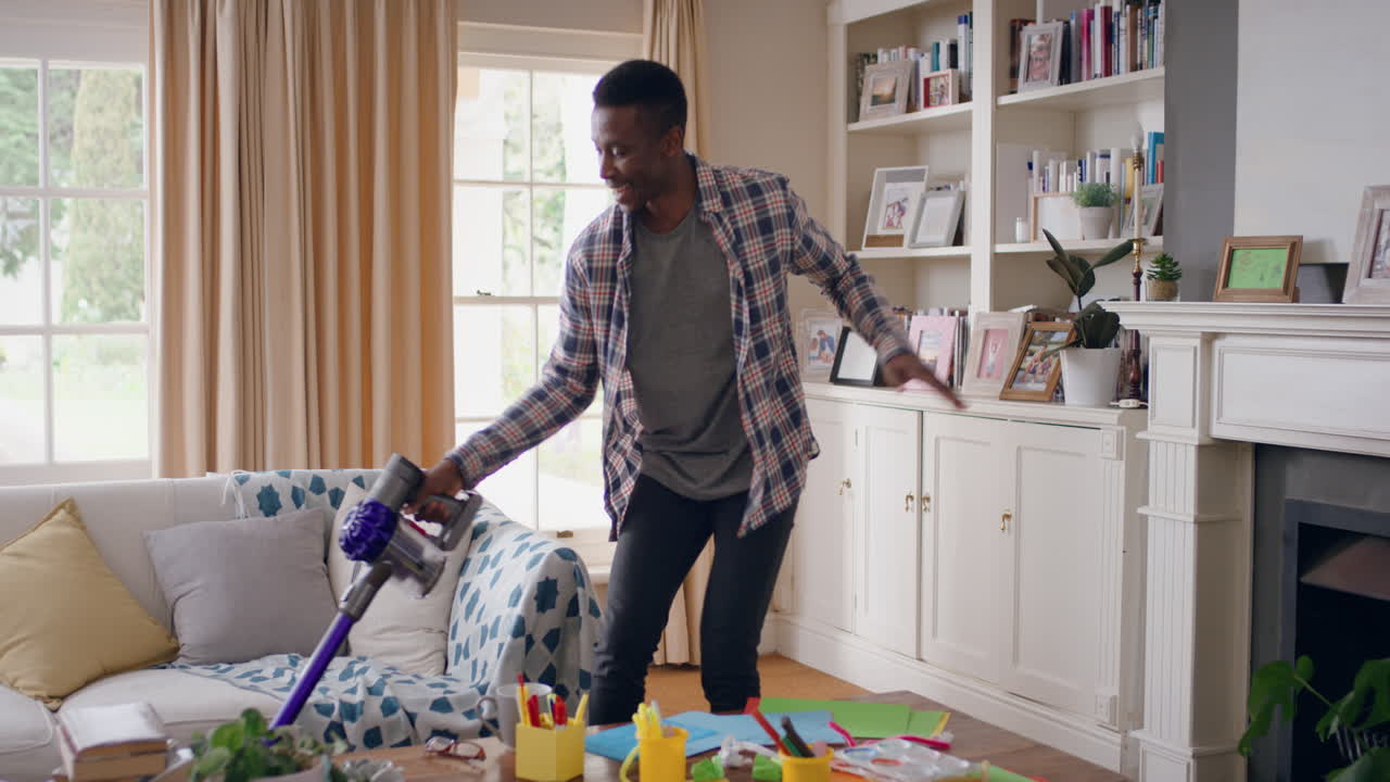 funny african american man dancing with vacuum cleaner at home celebrating success having fun dance cleaning living room doing chores on weekend 4k