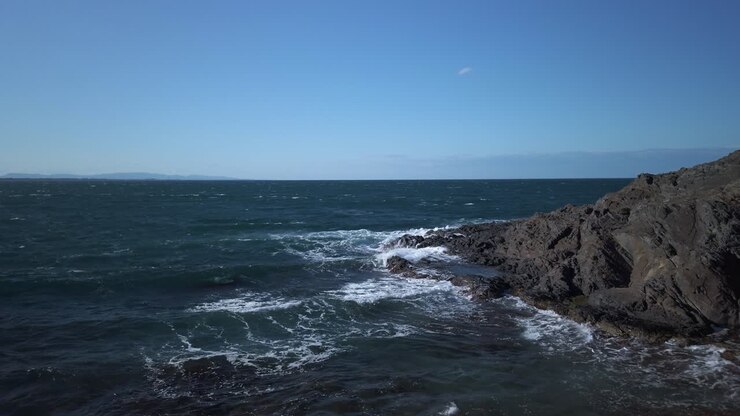 Il cielo azzurro abbraccia il blu intenso del Mar Mediterraneo mentre le sue onde accarezzano dolcemente la costa rocciosa di Collioure, Francia, creando un sereno paesaggio costiero.