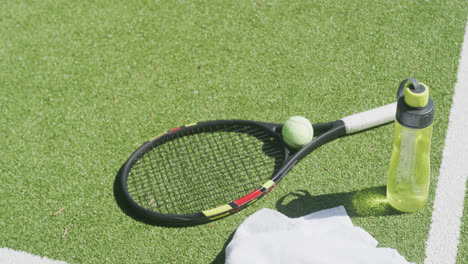 towel, bottle of water, tennis racket and ball lying on tennis court on sunny day