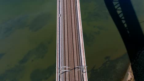 Flying over the center of the railway bridge over the marsh and the turquoise blue water of the Ulla River on a sunny day, rolling overhead drone shot up traveling forward, Catoira, Galicia, Spain