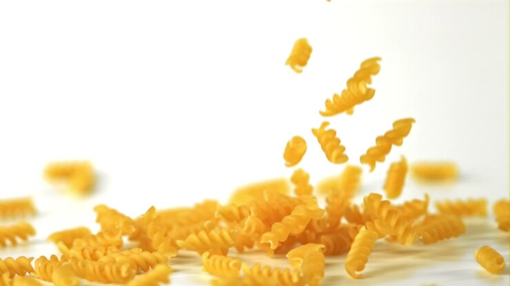 Pasta fusilli cruda che cade al rallentatore su sfondo bianco
