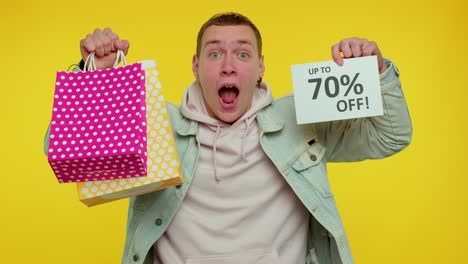 cheerful teen man showing shopping bags and up to 70 percent off inscriptions banner, black friday