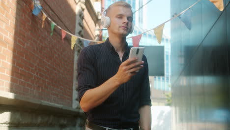 young man listening to music and using smartphone in urban street scene