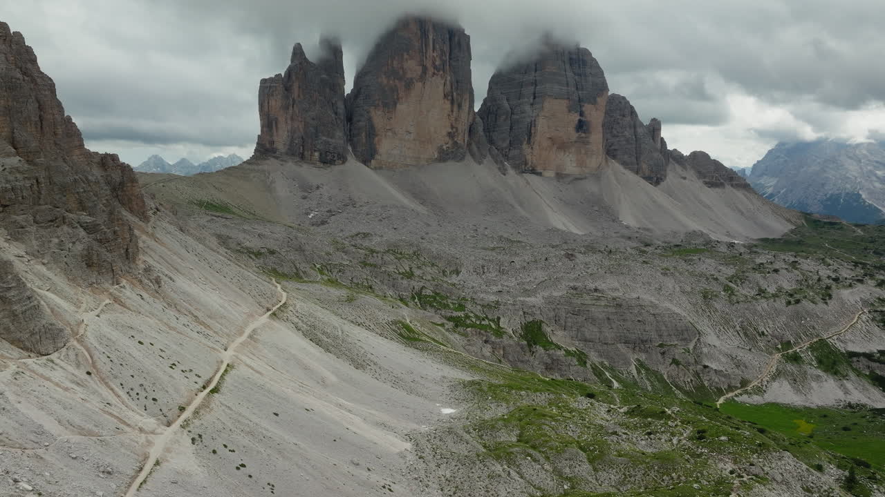 Sweeping aerial estabilshing of Tre Cime di Lavaredo with layered ridges and forested terrain below