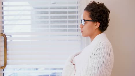 Woman-wrapped-in-shawl-looking-through-window-4k