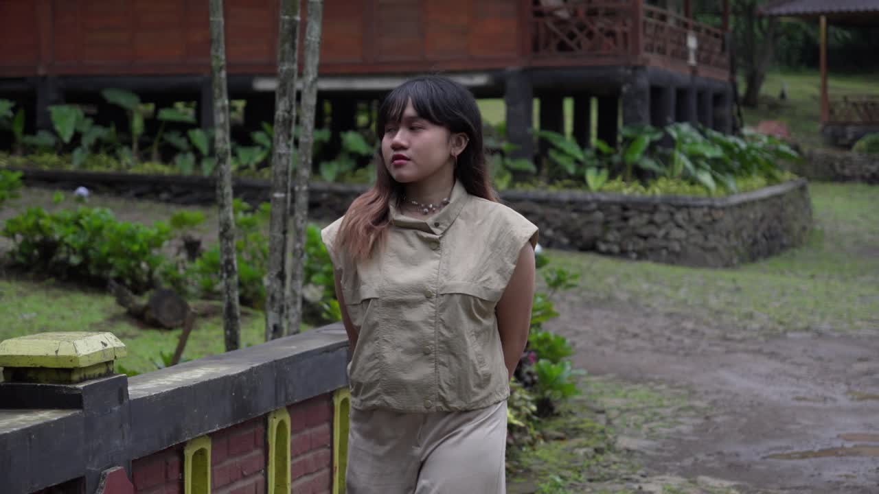 A young Indonesian woman walking near traditional houses surrounded by lush greenery
