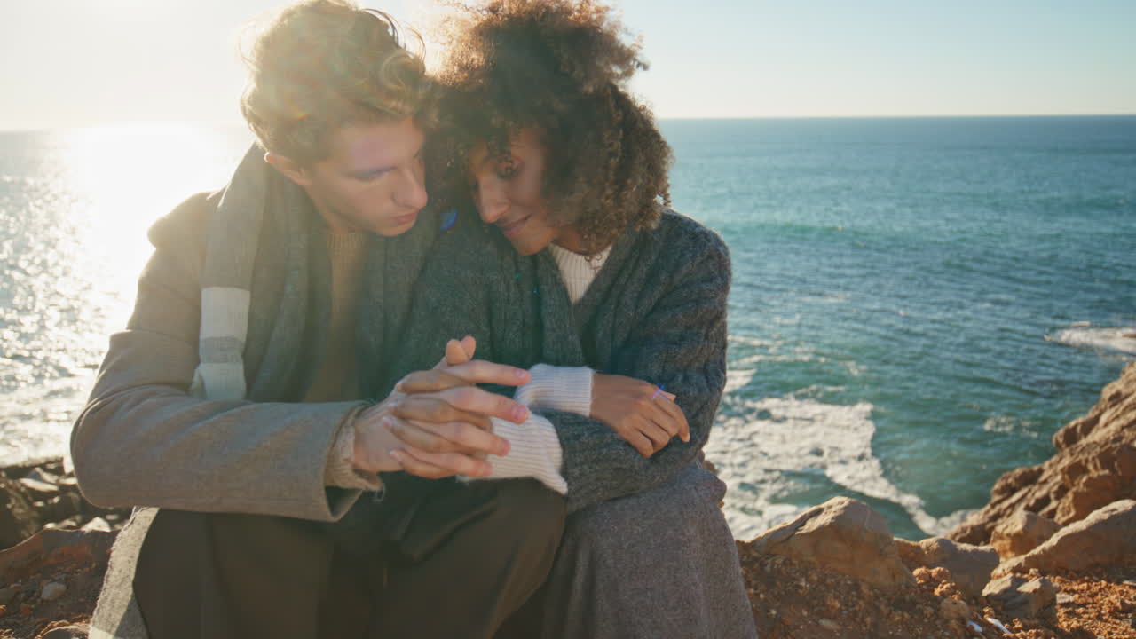 Affectionate lovers connecting hands sitting cliff at sea background closeup