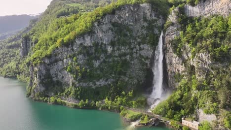 Seerenbach-Falls-cascading-down-a-rugged-cliff-into-the-turquoise-waters-of-Walensee,-surrounded-by-lush-greenery-in-Amden-Betlis,-Switzerland---aerial