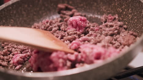 vista de cerca de una cuchara de madera revolviendo carne de res picada roja cruda en una sartén en la estufa con vapor - tiro estático en cámara lenta