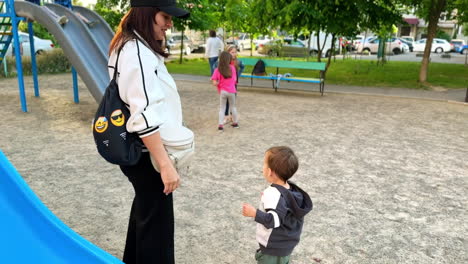 brunette woman playing with her baby on the playground. mother supporting her child as he slides down.