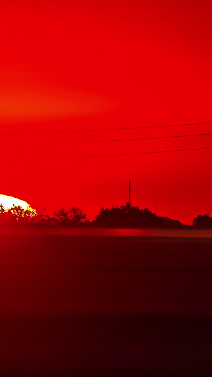 Red sky glows at sunset as birds fly across glowing horizon above foggy rural open field