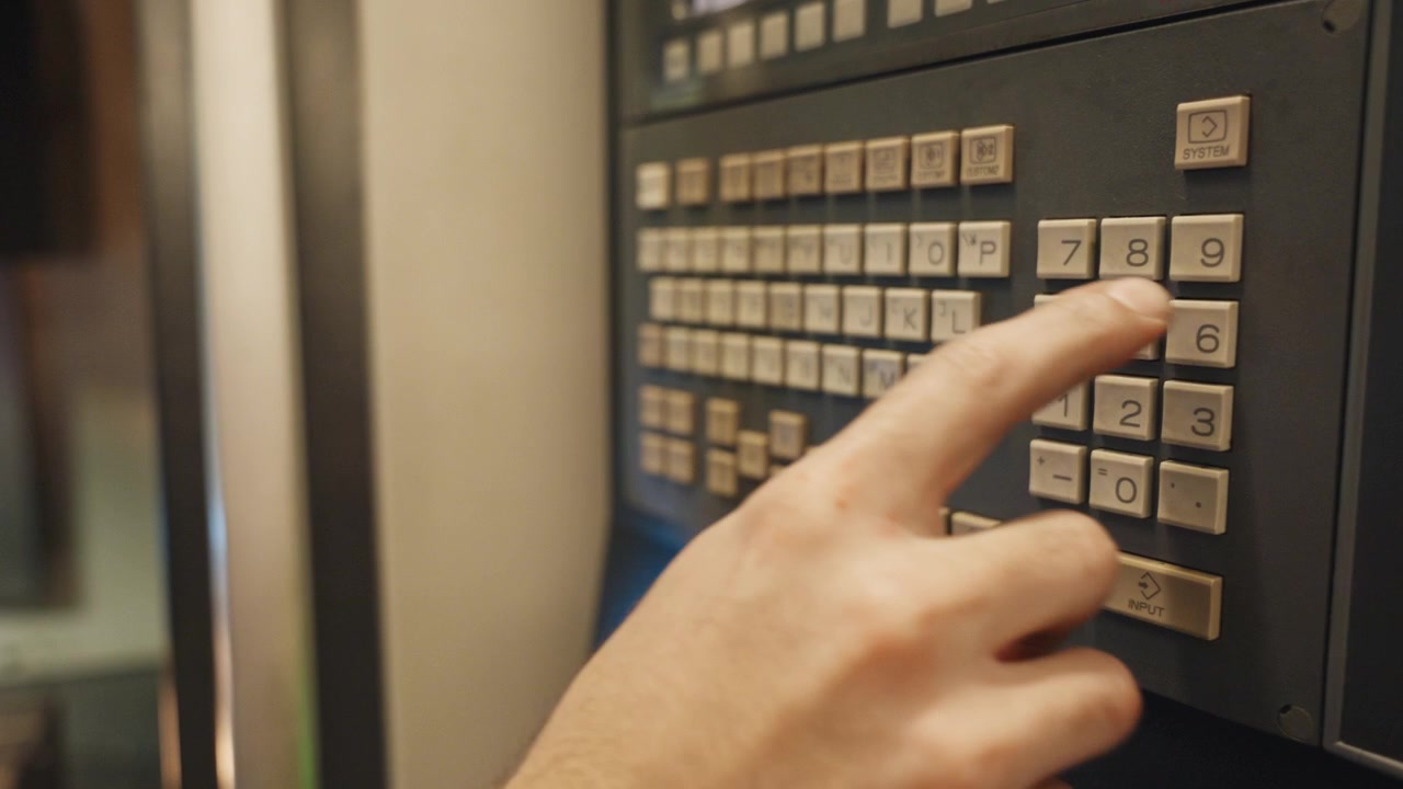 CNC operator presses control panel on machining center in factory, showing machine setup, industrial automation, production workflow, safety controls and modern manufacturing process.