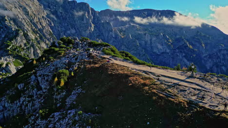 View-of-a-mountain-trail-with-hikers,-lush-greenery-and-rocky-terrain,-under-a-clear-blue-sky