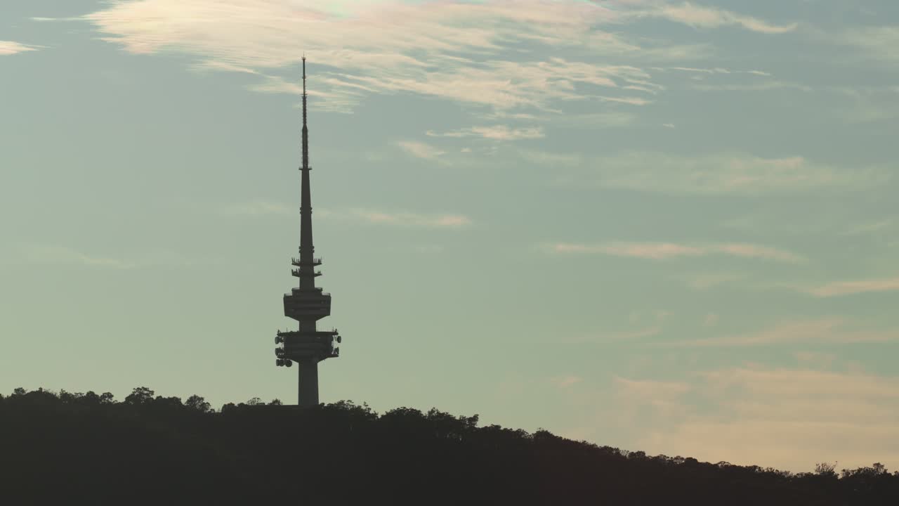 Slow zoom out reveals more of the morning sky around the silhouetted Canberra Tower in soft natural light