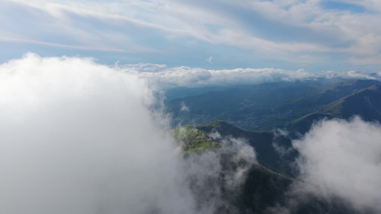 Big white clouds surrounding lush green mountain peaks, aerial view from above