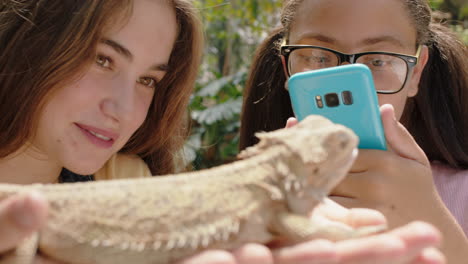 teenage girls holding iguana friends taking photos using smartphone sharing nature excursion on social media having fun learning about reptiles at zoo 4k