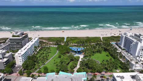 Aerial-lateral-shot-of-Miami-Beach-with-relaxing-people-on-sandy-beach-in-front-of-clear-ocean